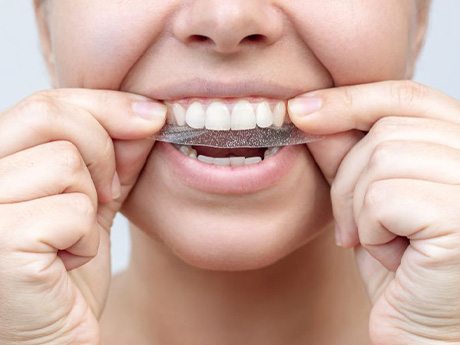 Woman applying teeth whitening strip to her teeth