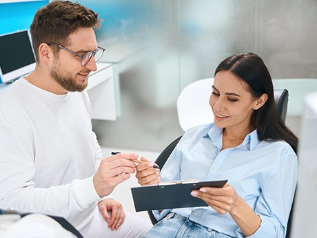 Man in white clothes handing forms to woman in dental chair