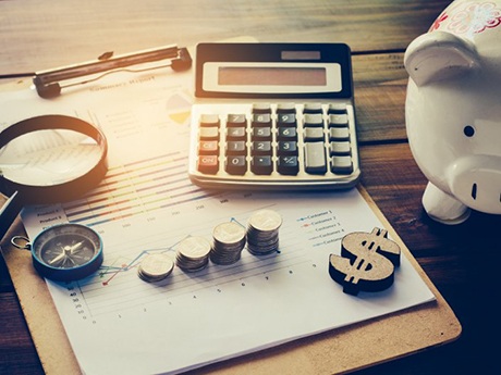 Calculator, coins, dollar sign, and piggy bank arranged on a desk