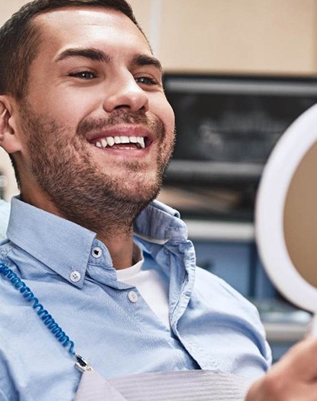 A smiling man looing at his treated teeth in a hand mirror