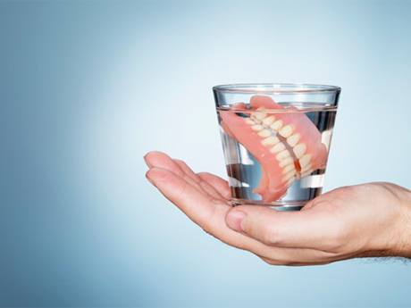 a person holding a cup of water with dentures