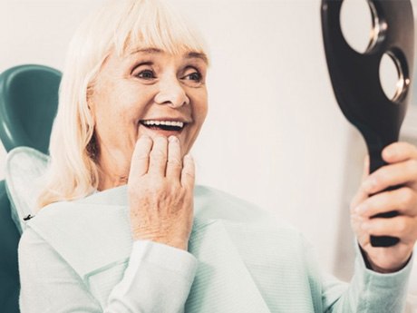 a woman checking her dentures with a mirror