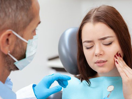 woman holding her cheek in pain in dental office