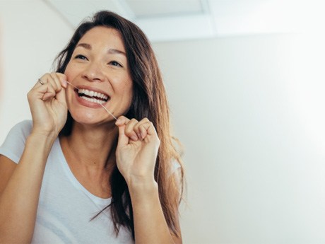 woman flossing teeth in mirror for prevent dental emergencies in Huntsville