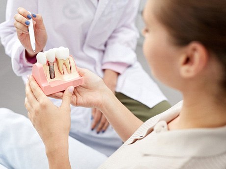 Dentist pointing to model of dental implant that patient is holding