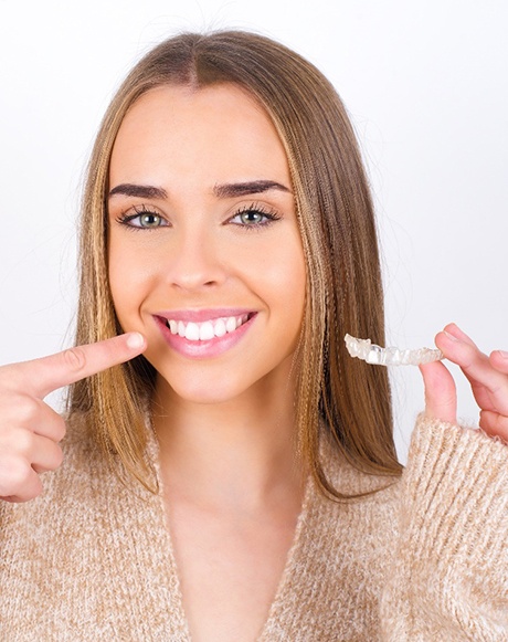 Young woman holding an Invisalign aligner and pointing at her teeth