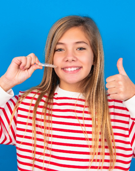 Girl in striped sweater holding Invisalign giving thumbs up