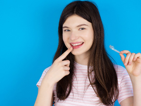 Girl in t-shirt holding Invisalign and pointing to her smile