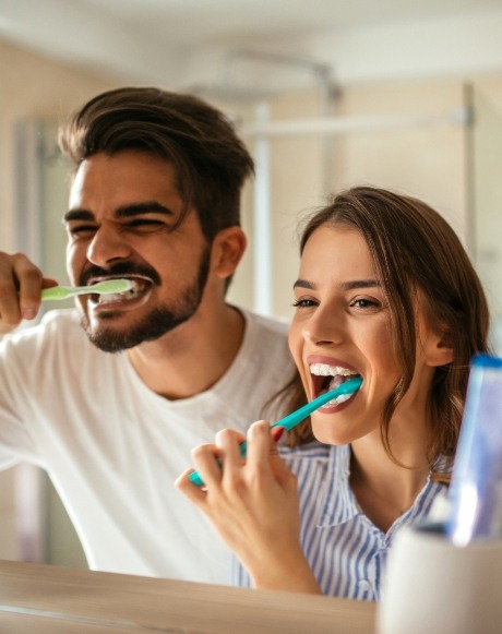 Man and woman brushing teeth between dental checkups and teeth cleanings