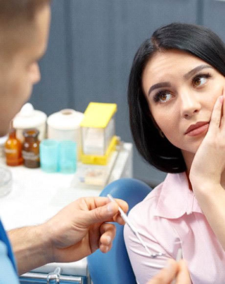 A woman looking at her dentist while holding her cheek in pain