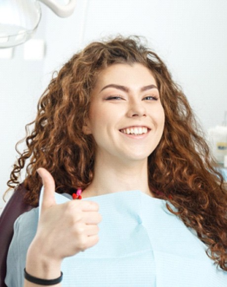 A smiling woman sitting in a dentist’s chair and giving a thumbs up