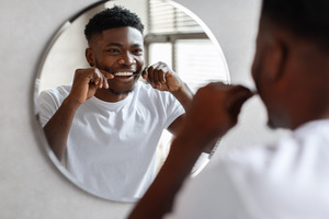 Man in white shirt flossing teeth in mirror